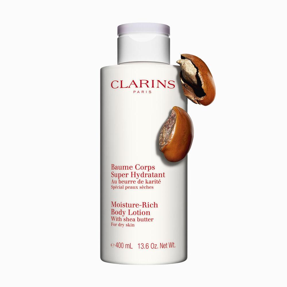 Packshot av en flaska med Clarins Moisture-Rich Body Lotion nära några sheanötter mot en vit bakgrund.