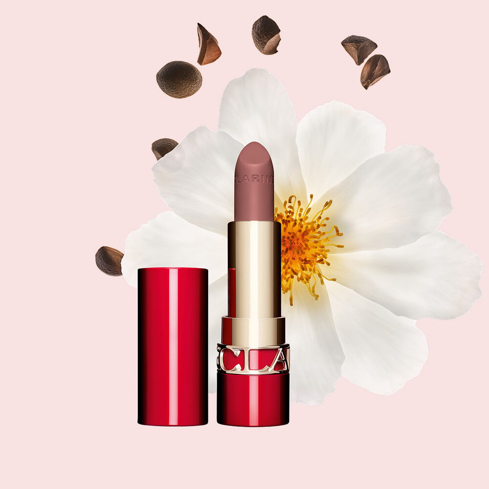 Packshot av Clarins matta l&auml;ppstift Joli Rouge i nyansen 795 V, placerat bredvid en kamelia blomma och sheafr&ouml;n p&aring; en rosa bakgrund.