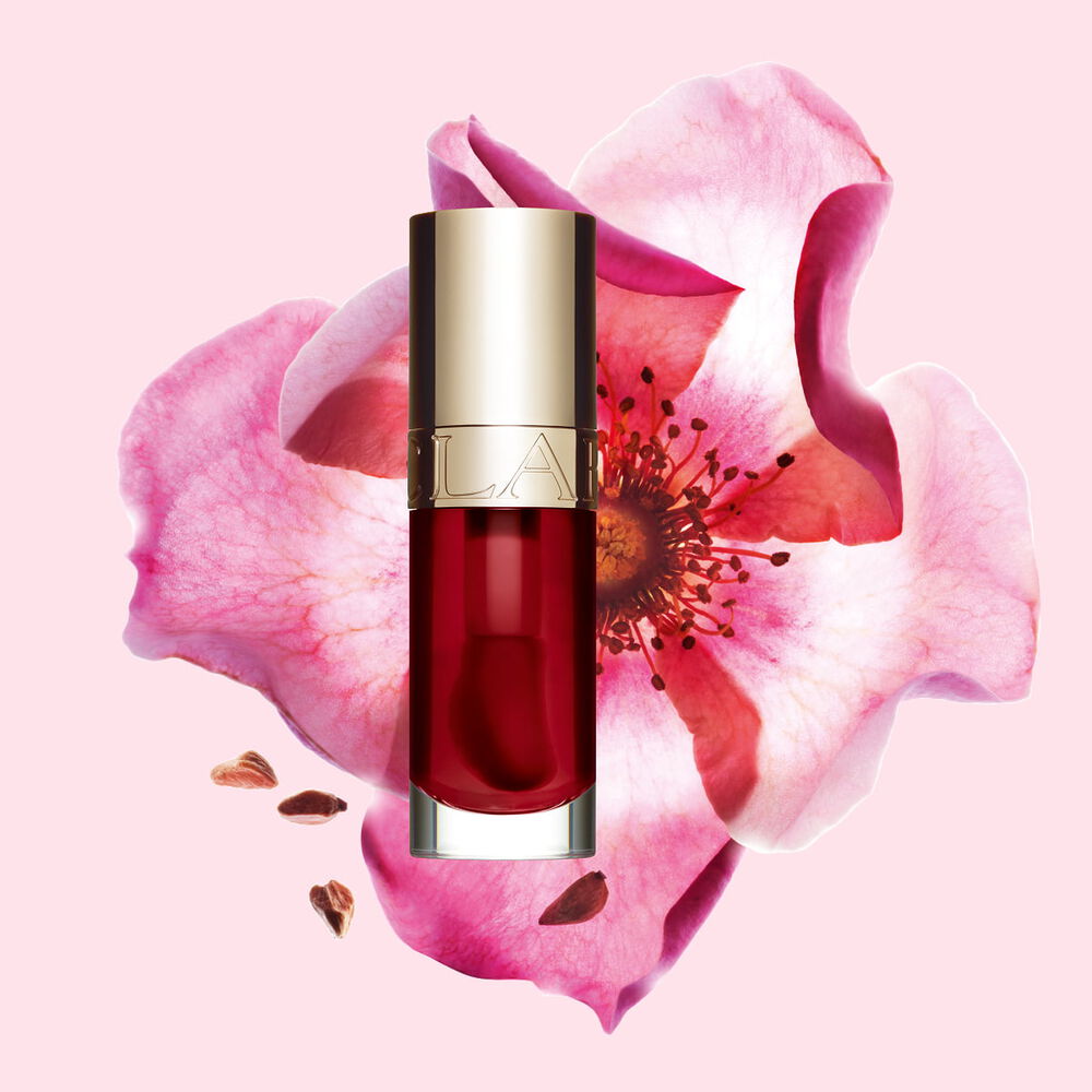 Packshot av Clarins Lip Comfort Oil i Cherry, placerad bredvid en nyponros p&aring; en ljus rosa bakgrund.