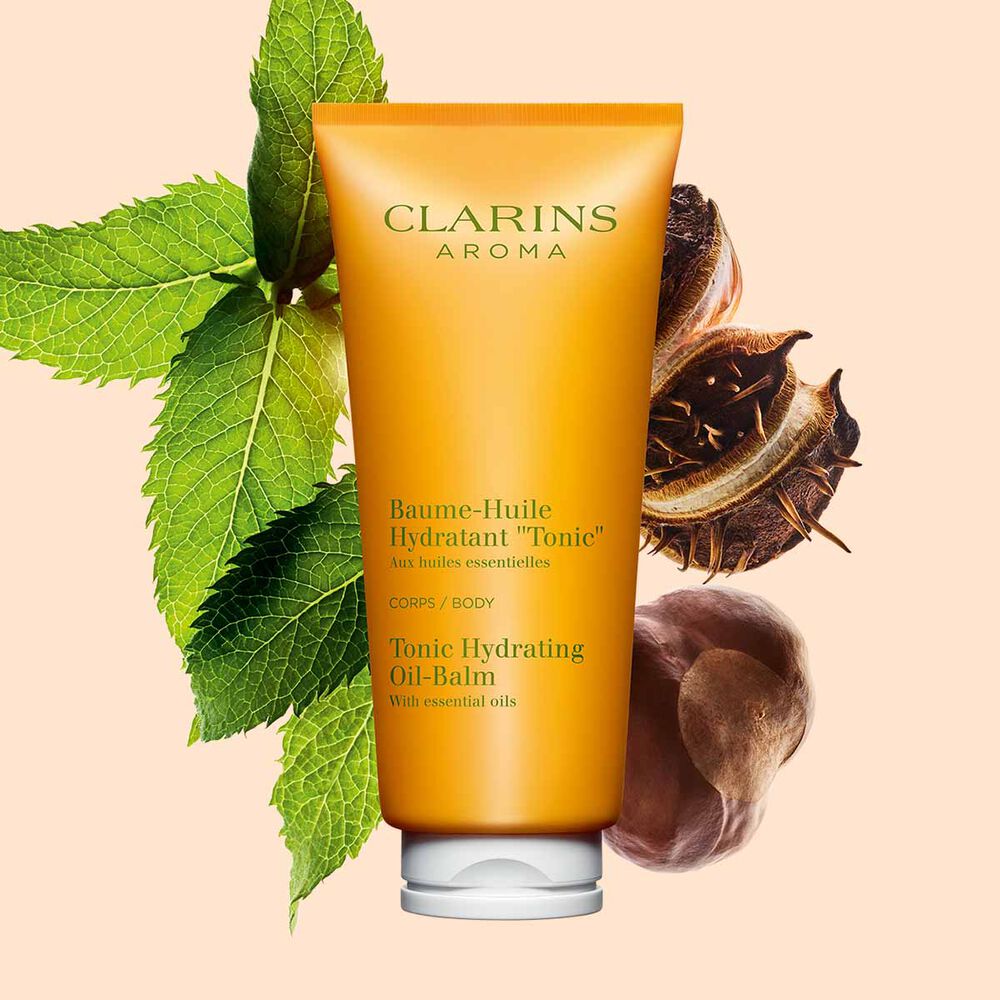 Packshot av en tub med Clarins Tonic Hydrating Oil-Balm, n&auml;ra n&aring;gra myntablad och shean&ouml;tter mot en persikof&auml;rgad bakgrund.