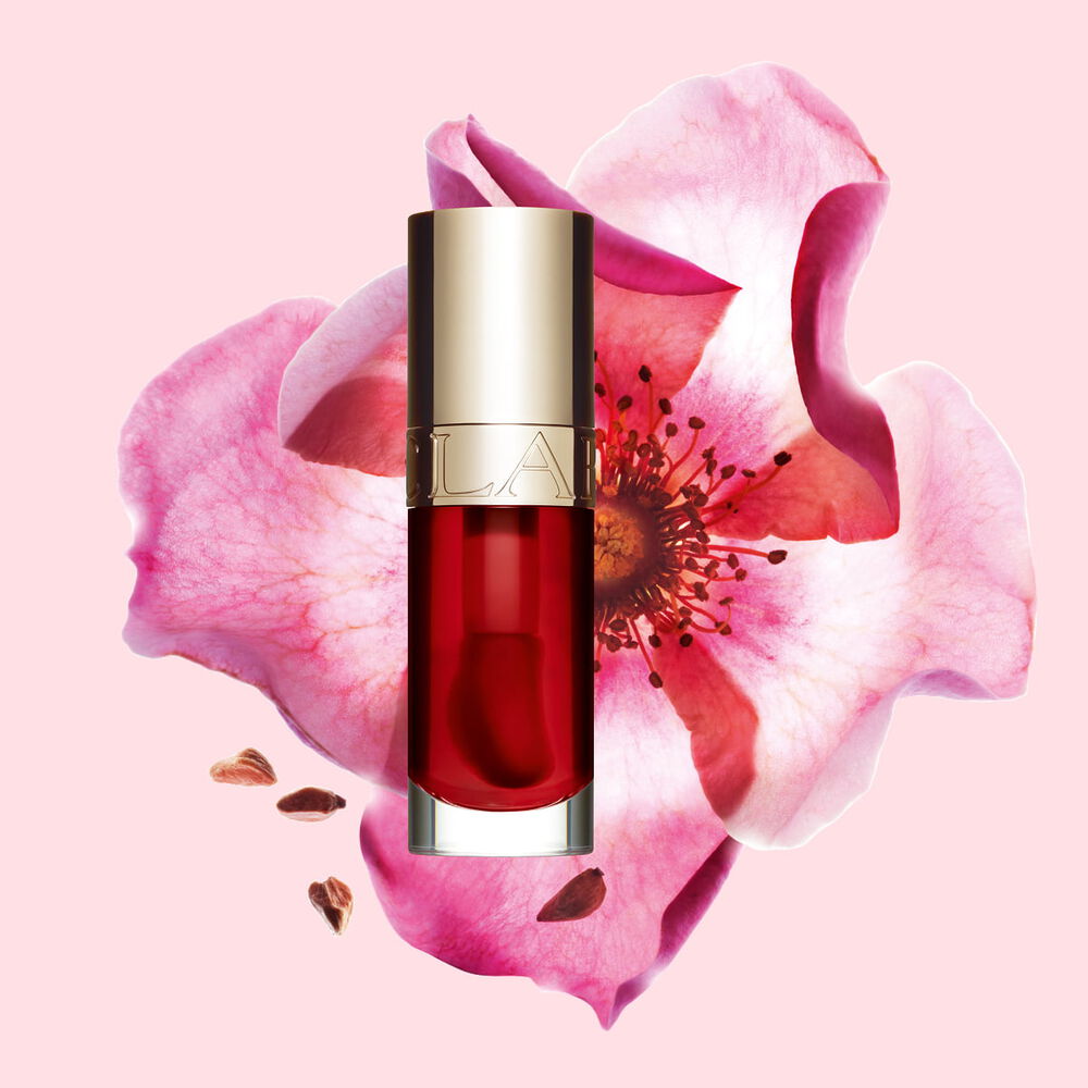 Packshot av Clarins Lip Comfort Oil Strawberry, placerad bredvid en nyponros p&aring; en ljusrosa bakgrund.