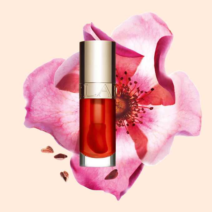 Packshot av Clarins Lip Comfort Oil i Apricot, placerad bredvid en nyponros p&aring; en ljus orange-pesikof&auml;rgad bakgrund.
