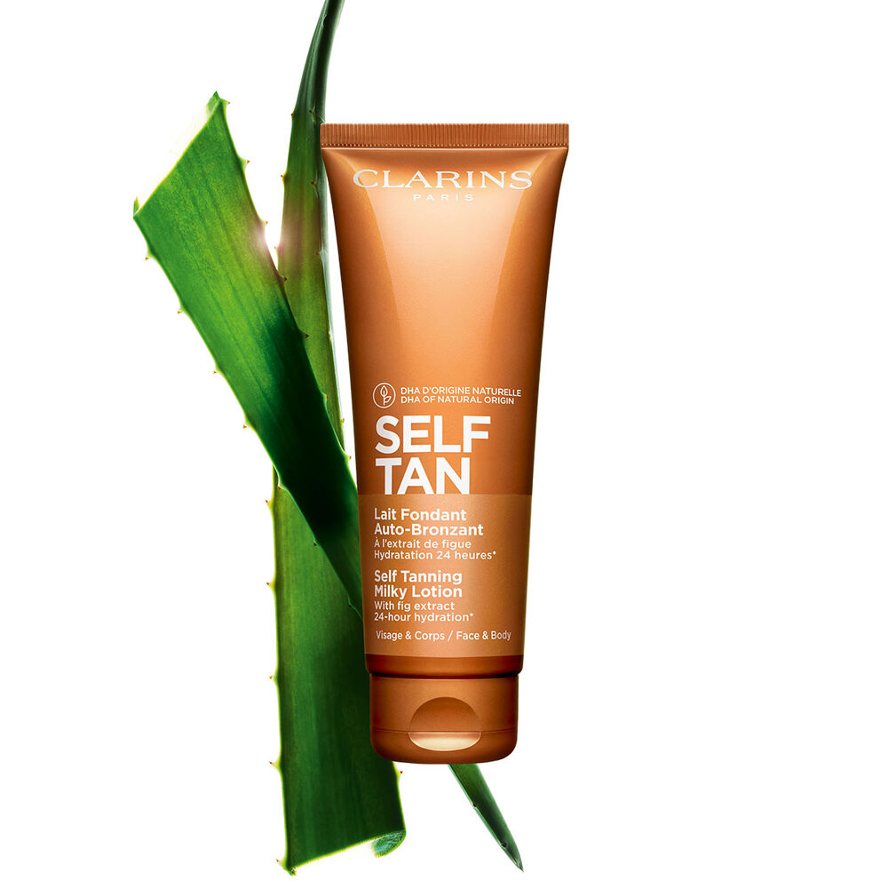 Packshot av en tub med Clarins Self Tanning Milky Lotion n&auml;ra lite aloe vera mot en ljust orange bakgrund.