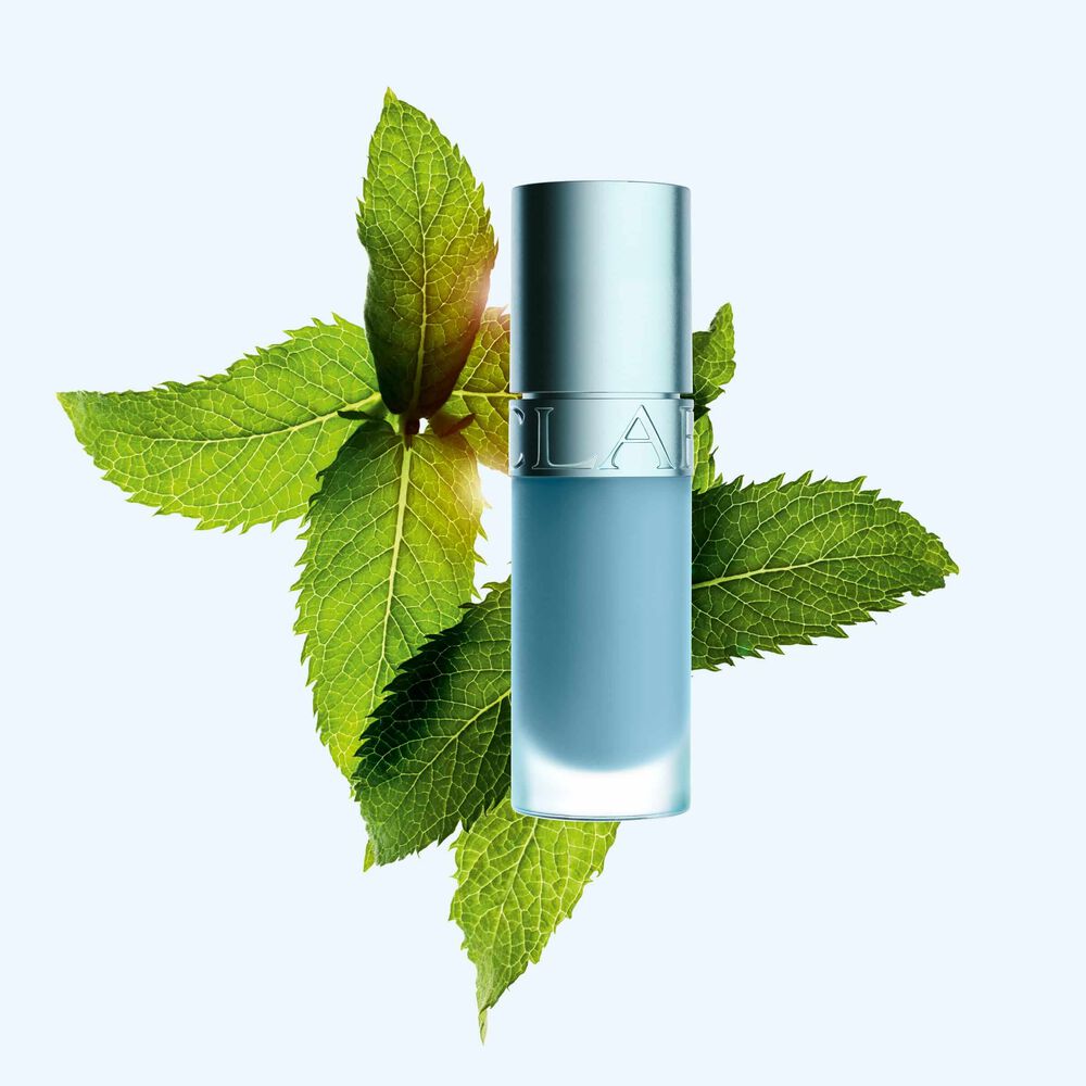 Packshot av Clarins Lip Comfort Oil med ny svalkande effekt och glansig finish, placerad framf&ouml;r mynta f&ouml;r att framh&auml;va dess nyckelingrediens
