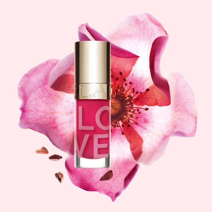 Produktbild av Lip Oil Limited Edition Love Collection framf&ouml;r en ros p&aring; en ljusrosa bakgrund som framh&auml;ver den livfulla f&auml;rgen.