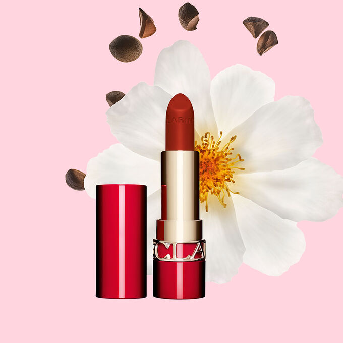 Packshot av Clarins matta l&auml;ppstift Joli Rouge i nyansen 782 V, placerat bredvid en kamelia blomma och sheafr&ouml;n p&aring; en rosa bakgrund.