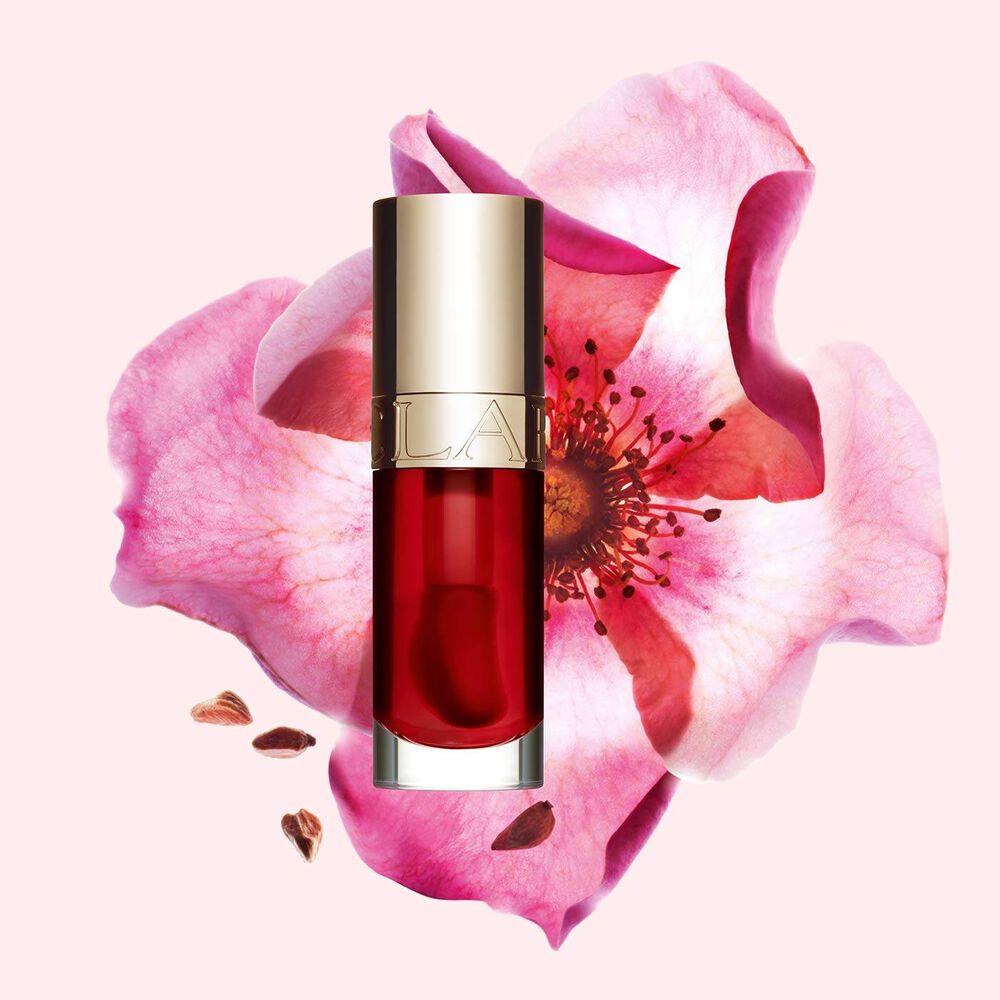 Packshot av Clarins Lip Comfort Oil Strawberry, placerad bredvid en nyponros p&aring; en ljusrosa bakgrund.
