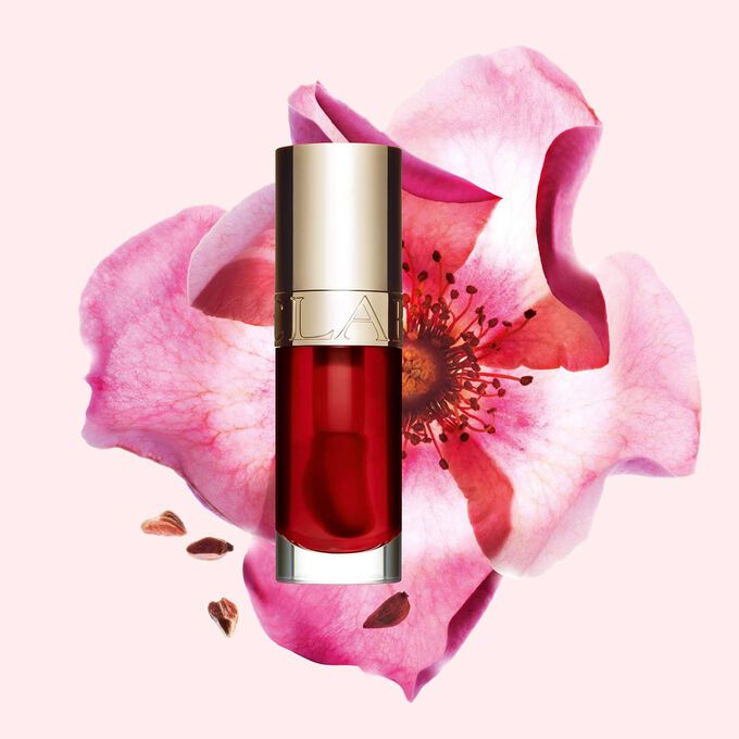 Packshot av Clarins Lip Comfort Oil Strawberry, placerad bredvid en nyponros p&aring; en ljusrosa bakgrund.