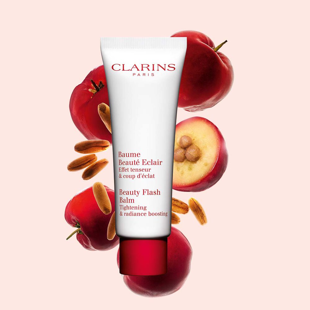 Packshot av en tub med Clarins Beauty Flash Balm nära acerolabär mot en persikofärgad bakgrund.