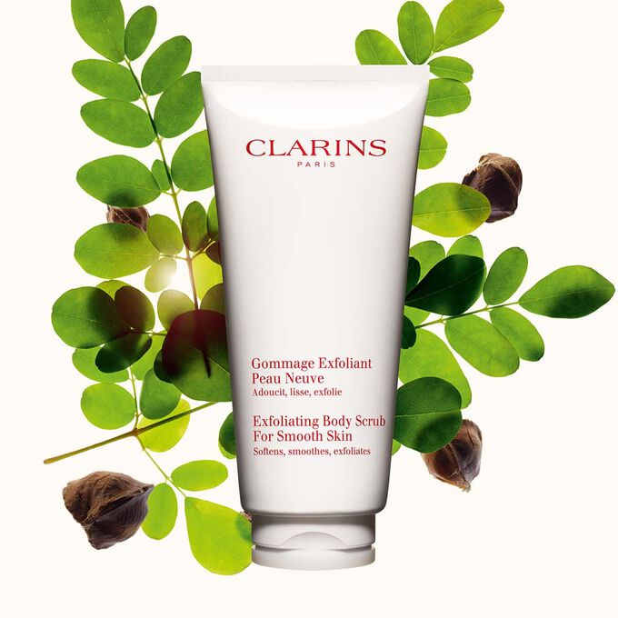 Packshot av Clarins Exfoliating Body Scrub for Smooth Skin, placerad bredvid moringan&ouml;tter mot en ljusbeige bakgrund