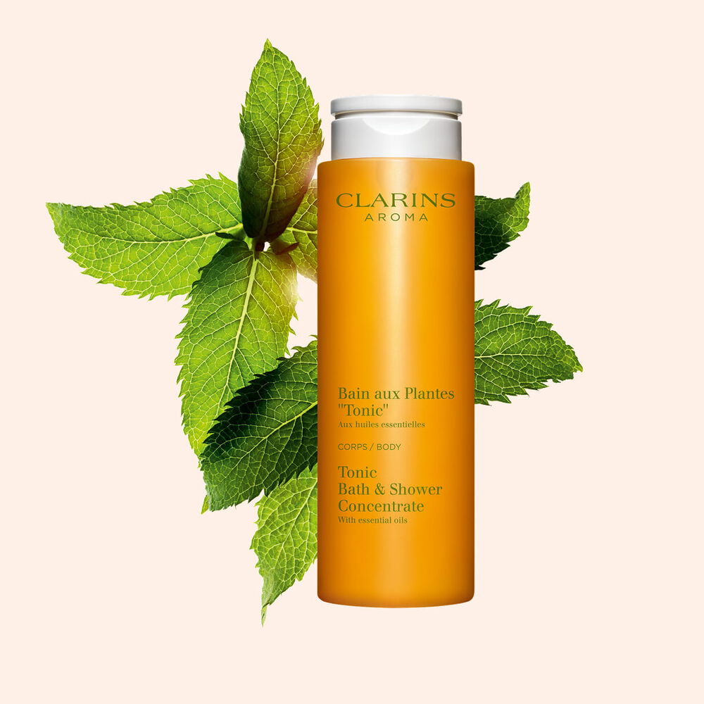 Packshot av duschgelen Clarins Tonic Bath & Shower Concentrate n&auml;ra blad av mynta och rosmarin mot en orange bakgrund.