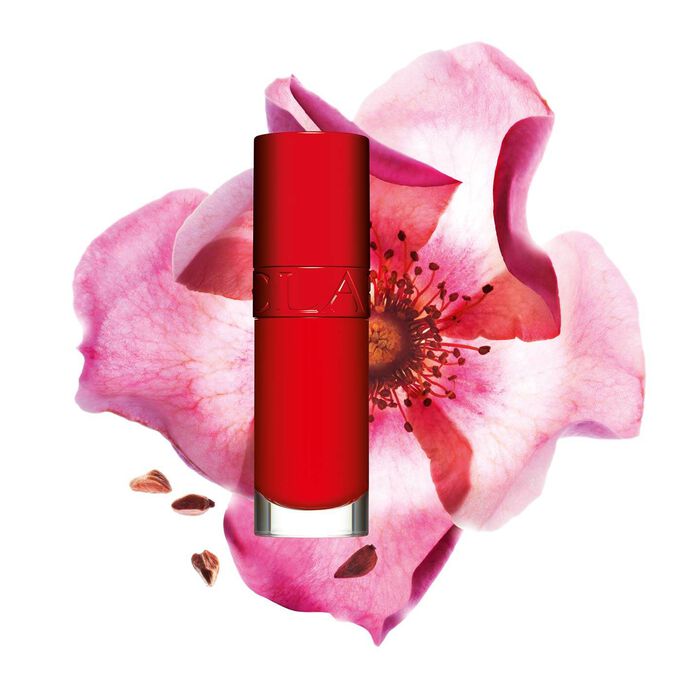 Packshot av Clarins Lip Comfort Oil i Iconic Red, placerad bredvid en nyponros blomma på en svart-röd bakgrund.