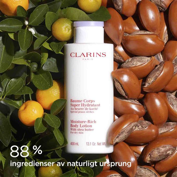 Flaska av Clarins Moisture-Rich Body Lotion omgiven av sheanötter och apelsiner för att illustrera dess naturliga ingredienser.