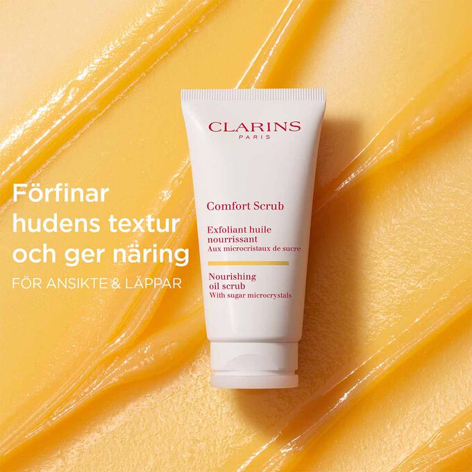 Clarins Comfort Scrub f&ouml;r ansikte och l&auml;ppar p&aring; en orange, texturerad bakgrund som framh&auml;ver dess f&ouml;rfinande och n&auml;rande effekt.